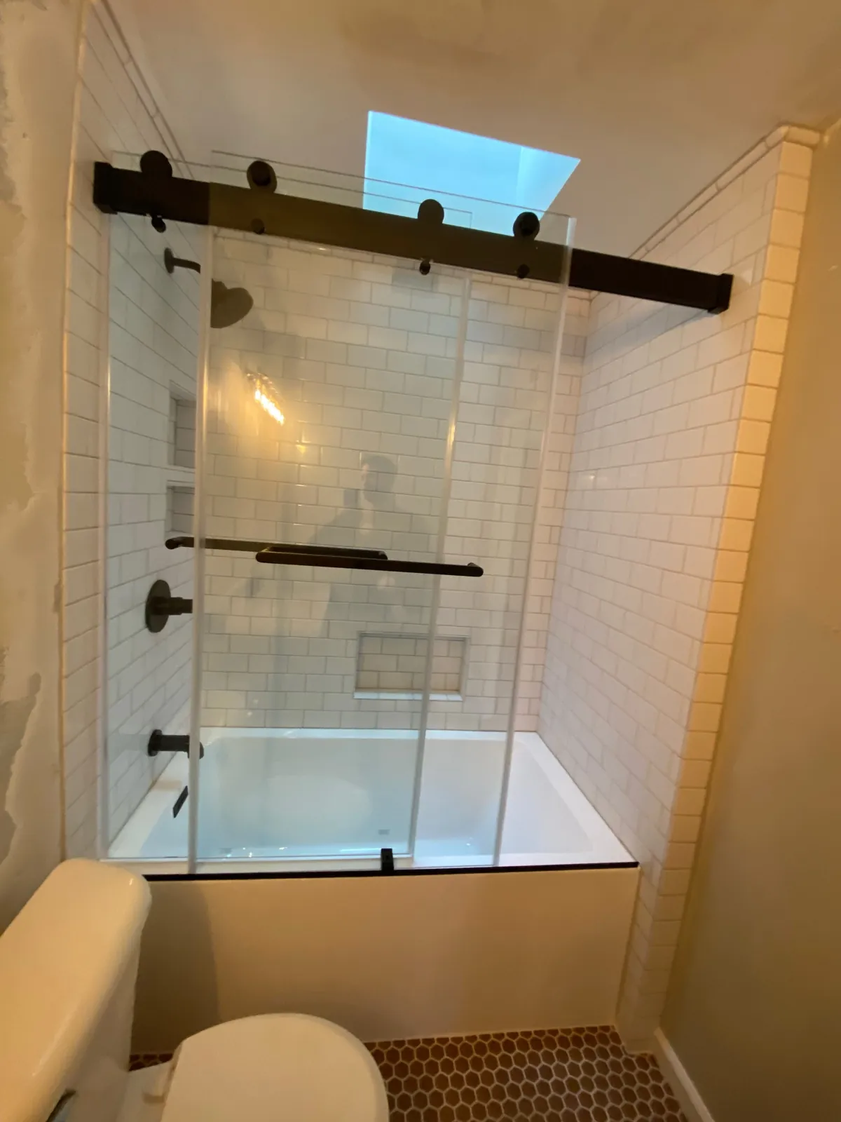 Subway tile tub shower with sliding glass door and skylight